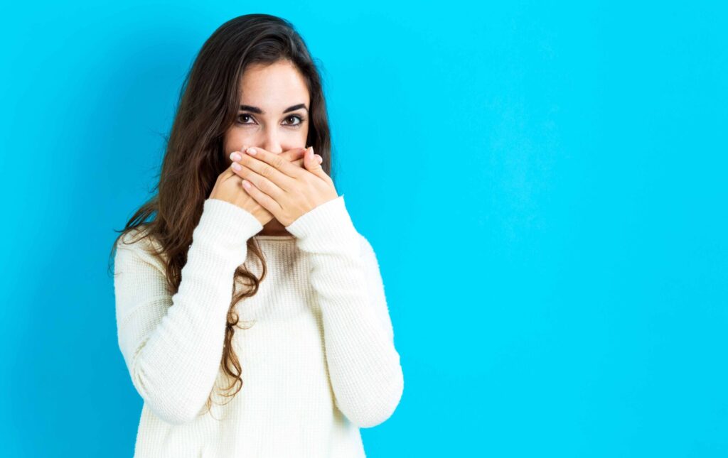 白いセーターを着た女性が口のもとを隠している