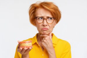 歯科医師の指示で入れ歯を外さない場合もあるのか入れ歯を片手に考えているシニア女性