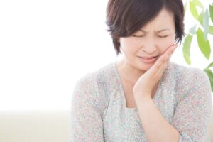 インプラント治療で痛みを感じて頬をおさえる女性
